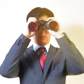 A man in a suit looking through a pair of binoculars 