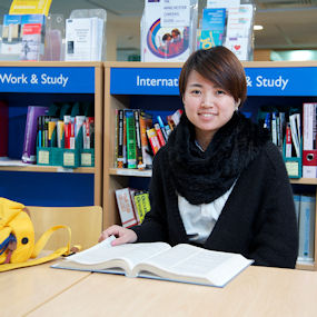 Female student sat with a book open in front of her smiling to camera