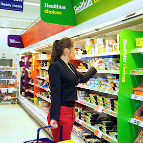 A young woman in a supermarket buying from an aisle marked 'healthier choices' 