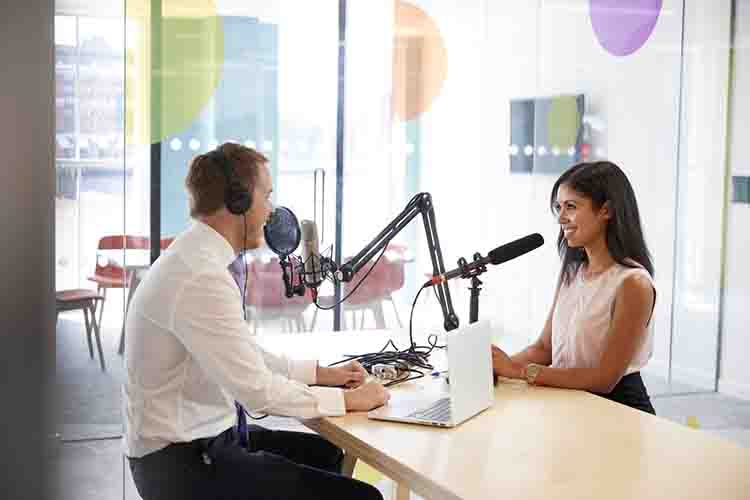 Man and woman having a radio interview across a table - microphones set up in front of them