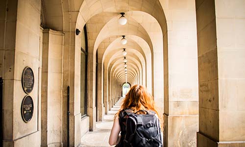 Landscape image of a student walking under a series of archways with an arrow on the wall