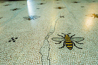 A tiled floor within an University building with a repeating pattern of the 'Manchester bee'.