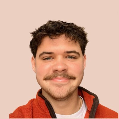 A picture of Theo Abbot, a student partner. He has brown short hair, has a moustache and is wearing a red jumper.