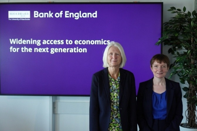 Image of Prof Fiona Devine and the Deputy Governor of Bank of England standing together infront of a presentation sign saying 'Widening access to economics for the next generation'