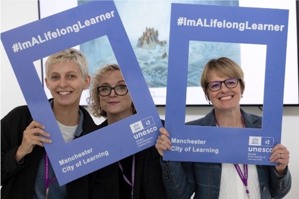 Image of three ladies holding up two lilac cardboard cutout frames saying 'lifelong learners'