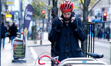 Man pulling up his coat collar as he prepares to get on a bike. 