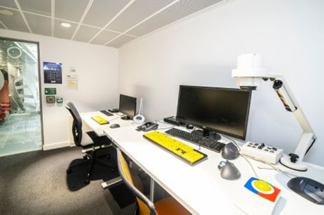 Accessible study room with two desks, monitors, high-contrast keyboards, assistive tech, and a desktop video magnifier.