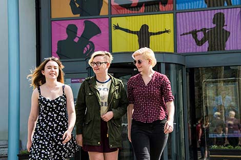 Three students walking together arm in arm outside the Martin Harris Centre