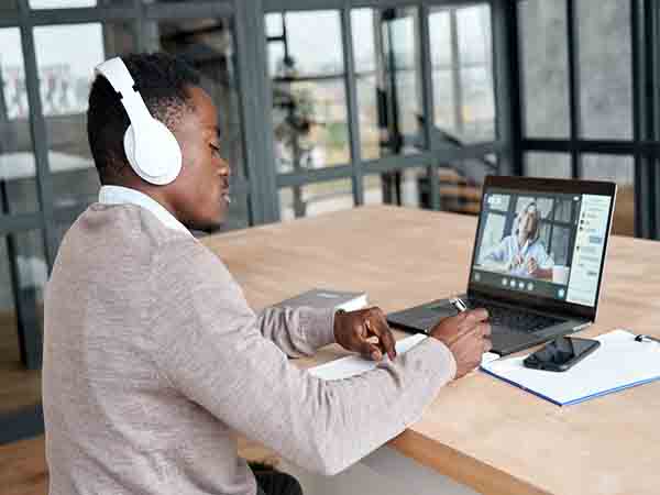 Man wearing headphones and working at a laptop displaying a video call