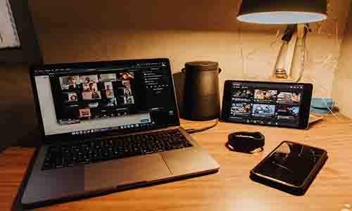 Desk with laptop showing a zoom call, tablet to the side displaying video resources and a mobile phone on the desk also. 