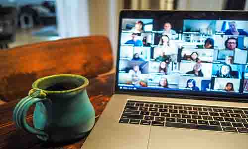 Laptop on a table, displaying a busy video call interaction, with a blue mug placed next to the laptop.