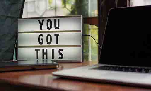Cinema style light-sign reading 'You got this' placed next to a computer of a table in front of a window 
