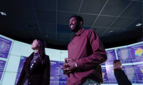 Image of two colleagues collaborating with a presentation in the background. 