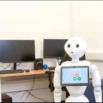 Image of white robot sat at computer desk