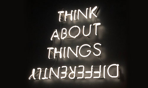 Neon sign reading 'Think about things differently' (with the word 'differently' rotated 180 degrees)