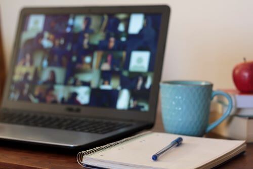 Laptop with group online meeting and blank notepad to the right