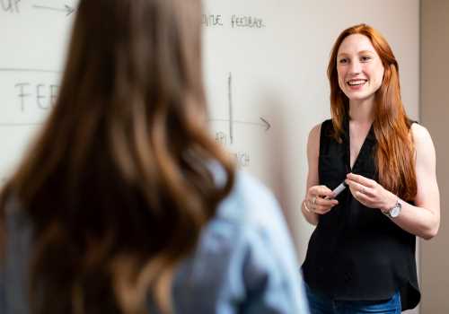 Woman stood by a white board talking to someone in front of her who has their back to the camera