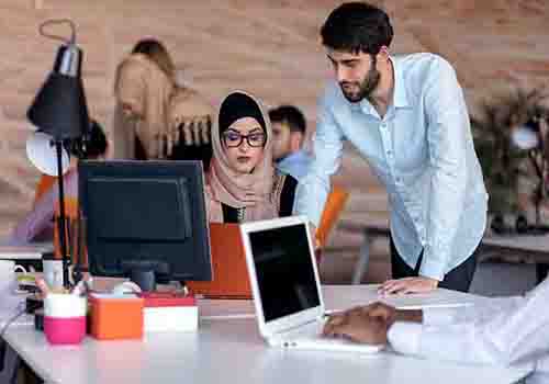 Male colleagues talking to a female colleagues and showing her something on her computer