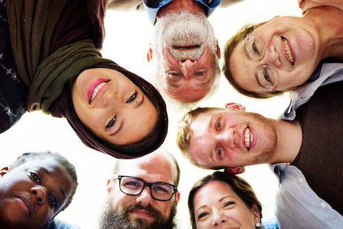 A group of people of diverse age ranges and ethnicities smiling and looking at the camera