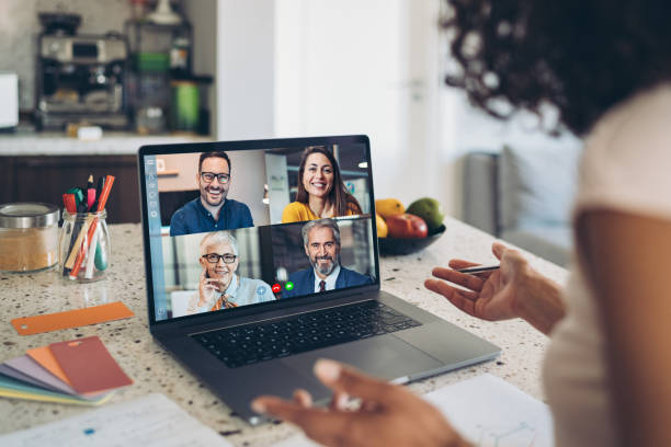 A woman working at a laptop from a home office, having a virtual meeting with four people.