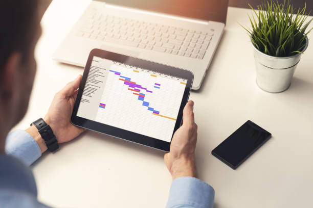 Man at a desk holding an ipad reviewing a project plan.