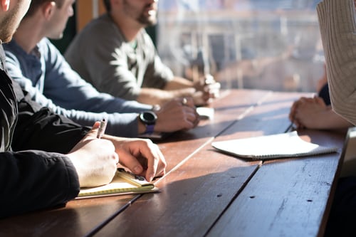 5 people sat at a table having a meeting with some paper in front of them