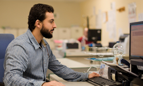 Image of bearded male sat working at computer in a lab
