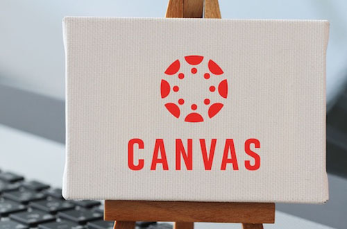 An easel and canvas with the Canvas logo on the canvas. The easel is in front of a laptop