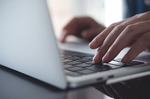 A woman typing on a laptop with a mobile phone next to her