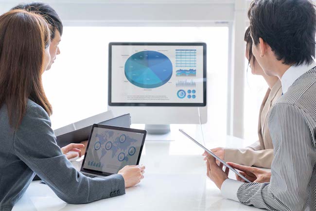 A team collaborate on a spreadsheet on a large monitor whilst updating a presentation on a tablet