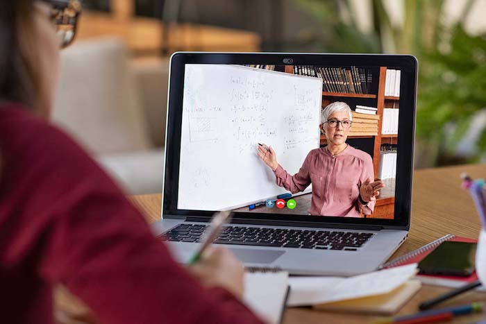 A student watches an online lecture of her lecturer in front of a white board which is covered in mathematical calculations