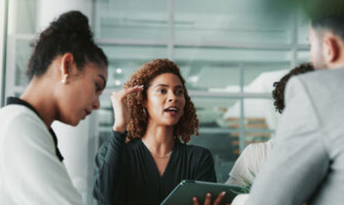 A woman holding a tablet speaking with colleagues