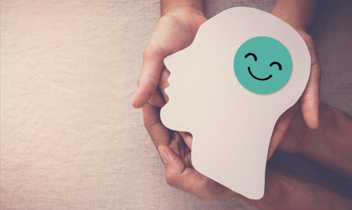 A pair of hands holding a cardboard cut-out of a head with a smiley face on it.