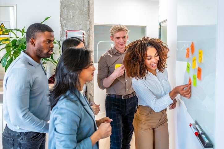 5 people looking at a whiteboard with post-it notes
