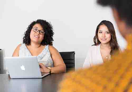 Two women talking to a person across the table from them who has their back to the camera