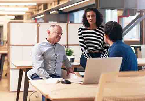Two men and at a woman talking around one desk