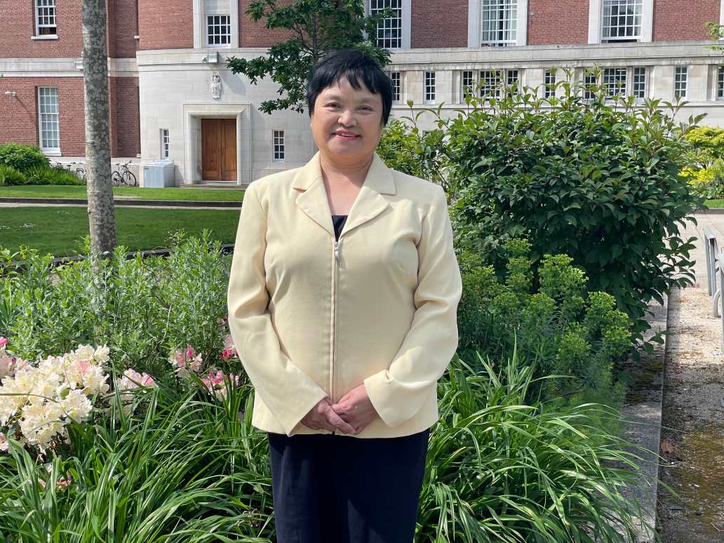 Photograph of Dr Minjie Xing smiling in the green garden area outside the Samuel Alexander Building 