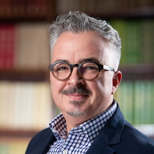 Photograph of Simon Thomson smiling with a bookcase in the background