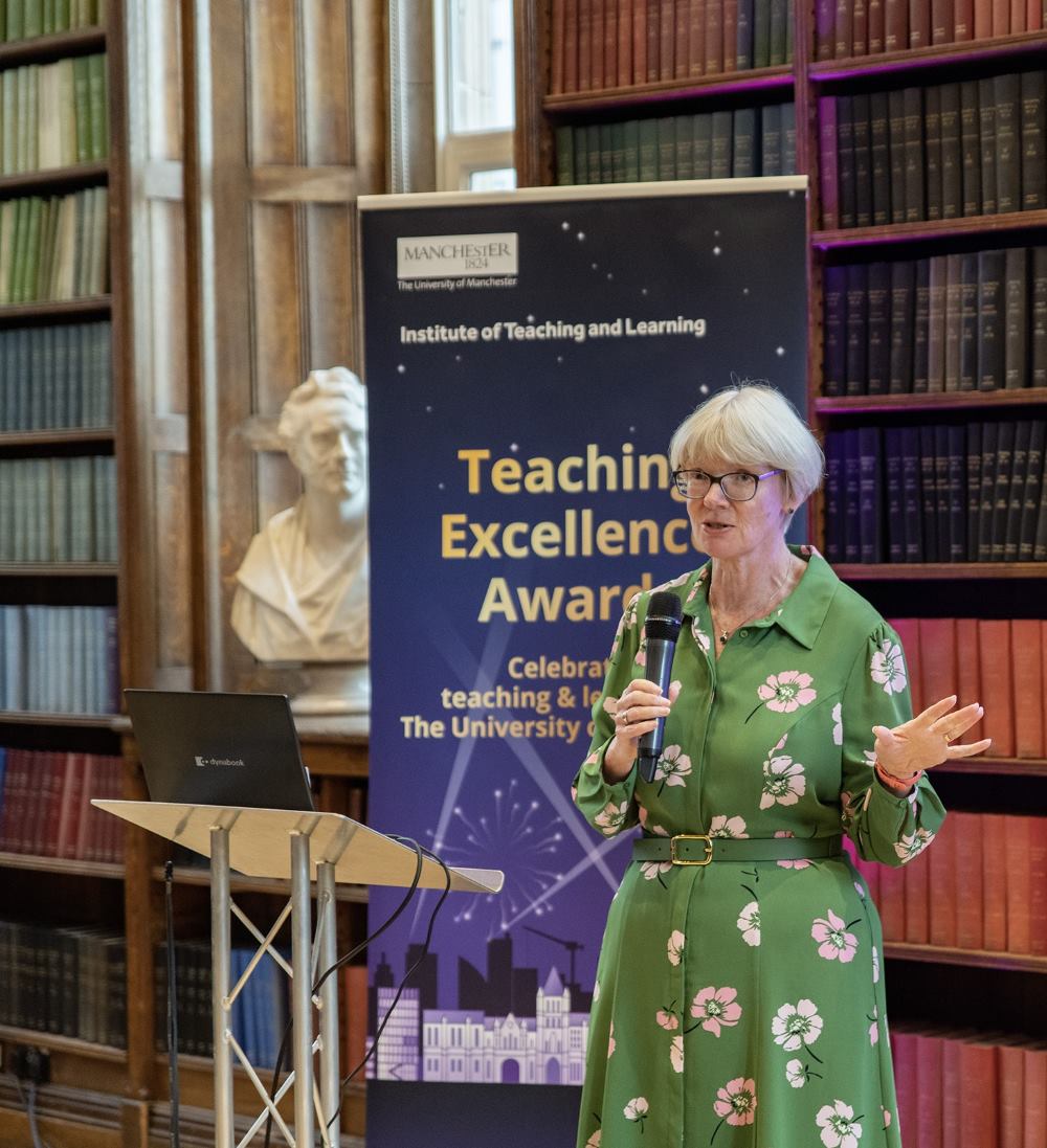 Professor April McMahon delivers a speech next to a Teaching Excellence Awards banner 