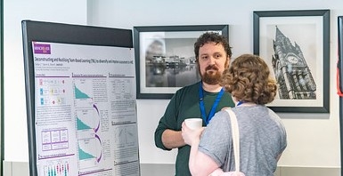 An image of a conversation in the Pioneer room about one of the poster presentations between the presenter and an attendee.
